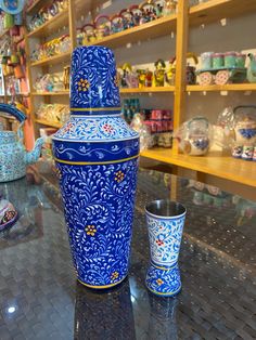 a blue and white vase sitting on top of a table next to a glass cup