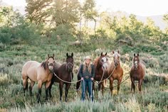 a woman leading four horses in a field