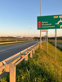 a highway sign on the side of a road with grass and bushes next to it