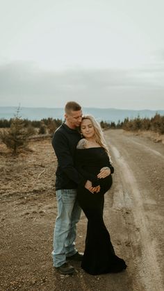 a pregnant couple standing in the middle of an empty road with their arms around each other