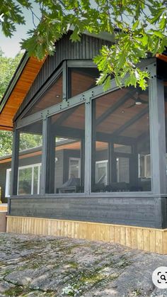 a house that is sitting under a tree with lots of windows on the side of it