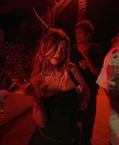 a woman in a black dress standing next to two other people at a party with red lights