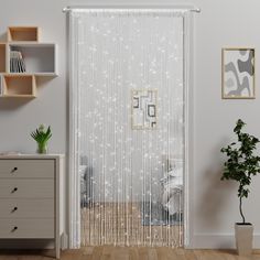 an open door with white curtains in a room next to a dresser and potted plant