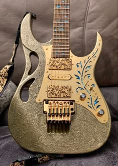 an electric guitar with gold and blue paint on it's body, sitting on a couch