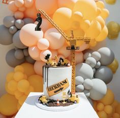 a construction themed birthday cake on a table with balloons in the background and a giant crane behind it