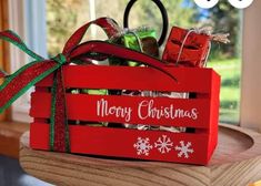 a wooden crate filled with christmas gifts on top of a table next to a window