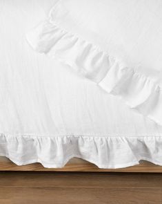 a bed with white sheets and ruffles on the bottom half, along with a wooden headboard