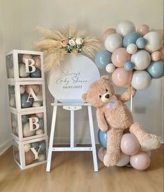 a teddy bear is sitting on a stool next to balloons and a sign that says baby