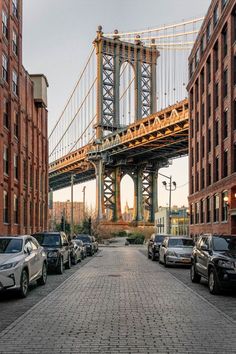 cars are parked on the street in front of tall buildings with a bridge above them