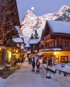 people are walking down the street in front of some buildings with mountains in the background