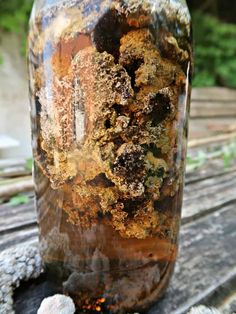 a jar filled with lots of dirt sitting on top of a wooden table next to a rock