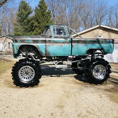 an old pick up truck is parked in front of a house with large tires on it