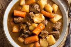 a white bowl filled with stew and carrots on top of a wooden table next to a fork