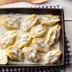 a baking pan filled with stuffed shells covered in gravy and topped with fresh herbs