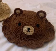 a crocheted teddy bear hat on top of a bed next to another stuffed animal