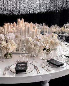 a white table topped with lots of plates and glasses filled with flowers next to candles