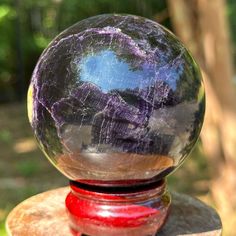 a glass ball sitting on top of a wooden table next to a green field and trees