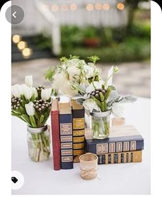 some books and flowers are sitting on a white tablecloth with candles in vases