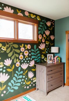 a bedroom with flowers painted on the wall next to a dresser and window in front of it