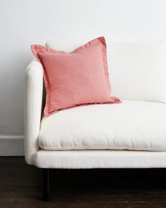 a white couch with a pink pillow on it next to a wooden floor and wall