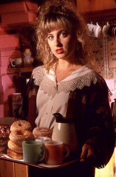 a woman holding a tray with donuts and cups on it in a kitchen area