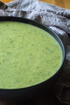 a black bowl filled with green soup on top of a wooden table next to a napkin