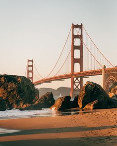 the golden gate bridge is over looking the water and rocks on the beach in front of it