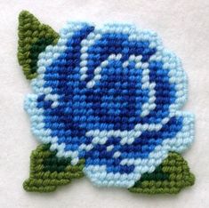 a blue flower with green leaves is shown on a white surface, and it appears to be crocheted