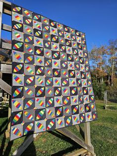 a large quilt is sitting on top of a wooden easel in the grass near a fence