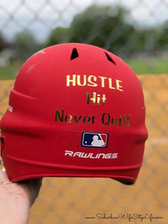 a red baseball helmet that says hustle hit never quit