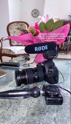 a video camera sitting on top of a table next to a bouquet of pink flowers