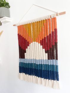 a wall hanging made out of multicolored beads and rope with a potted plant in the background