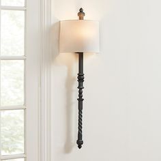 a wall mounted lamp with a white shade on it's side and a window in the background