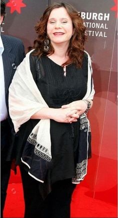 a woman standing in front of a red carpet with her arms crossed and wearing a shawl