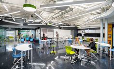 people are sitting at desks in an open area with lots of chairs and tables