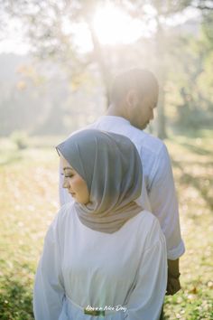 a man and woman are walking in the grass together, with sunlight shining on them