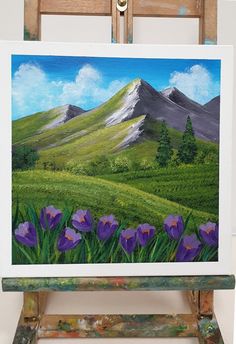 an easel is holding up a painting of purple flowers in front of a mountain