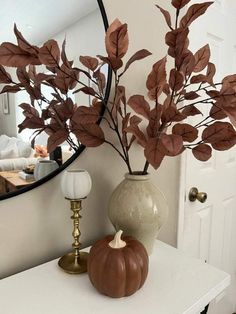 there is a mirror and vase with leaves on the table in front of it,