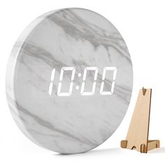 a marble clock with white numbers on it and a wooden stand in front of it