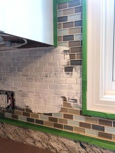 a kitchen with green and white tiles on the backsplash, counter tops and cabinets