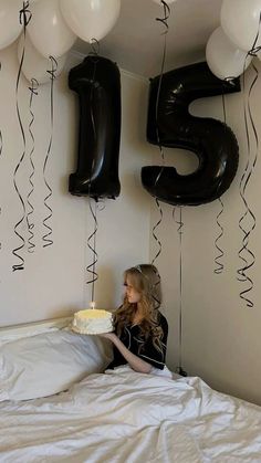 a woman sitting on a bed with balloons and a cake in front of the number five