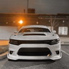 the front end of a white car parked in a parking lot at night with its lights on