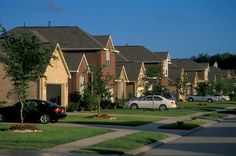 several cars parked on the side of a street in front of row houses with grass and trees