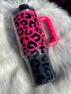 a pink and black leopard print water bottle sitting on top of a white furry surface