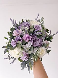 a hand holding a bouquet of flowers with greenery and lavenders on the stems