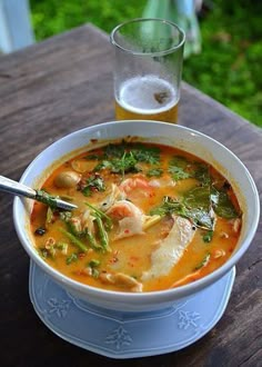 a white bowl filled with soup next to a glass of beer on top of a wooden table