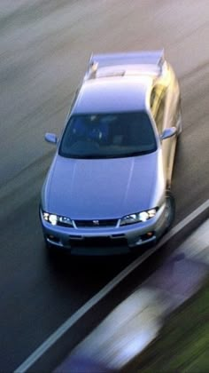 a silver car driving down a street next to grass