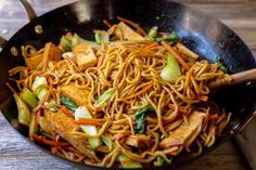 a wok filled with noodles and vegetables on top of a wooden table