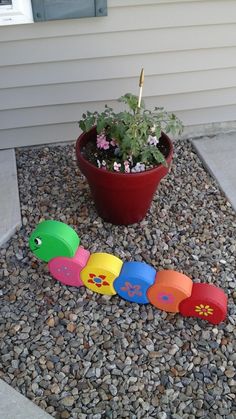 a toy train sitting on top of gravel next to a potted plant and flower