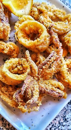 fried onion rings on a white plate with lemon wedges and seasoning sprinkles